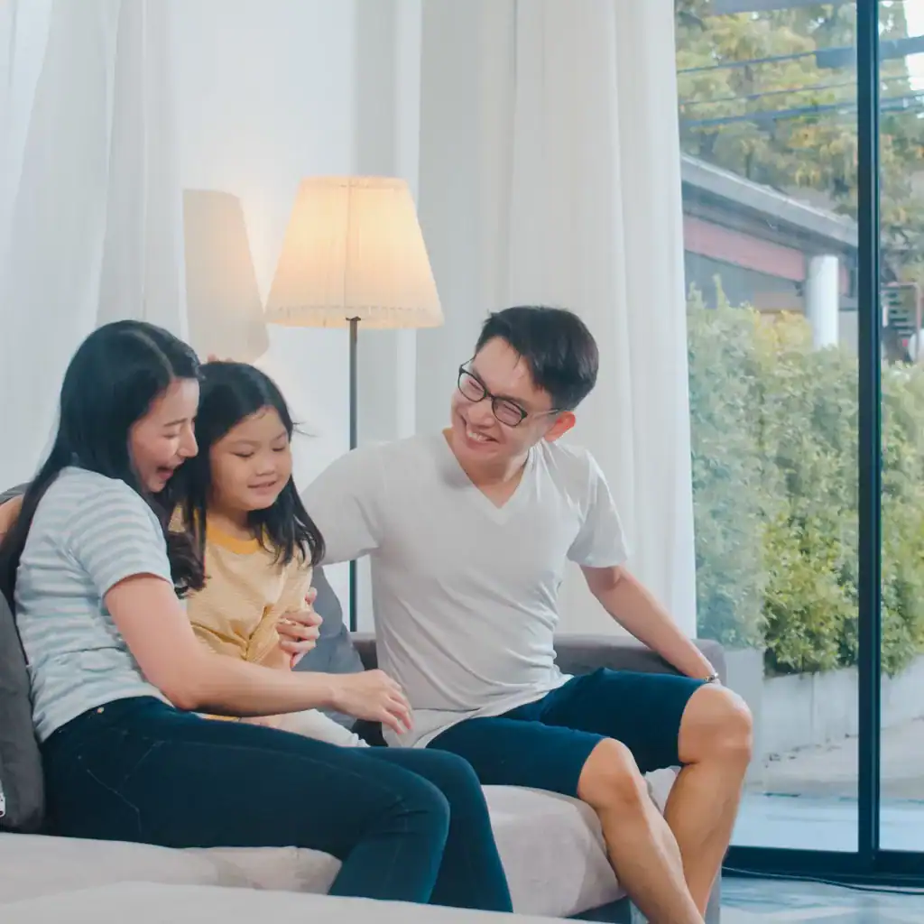 Happy young Asian family play together on couch at home. Chinese mother father and child daughter enjoying happy relax spending time together in modern living room in evening.
